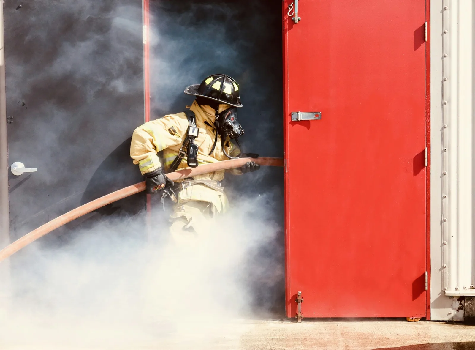 Firefighter in full gear advancing a charged hose line through smoke